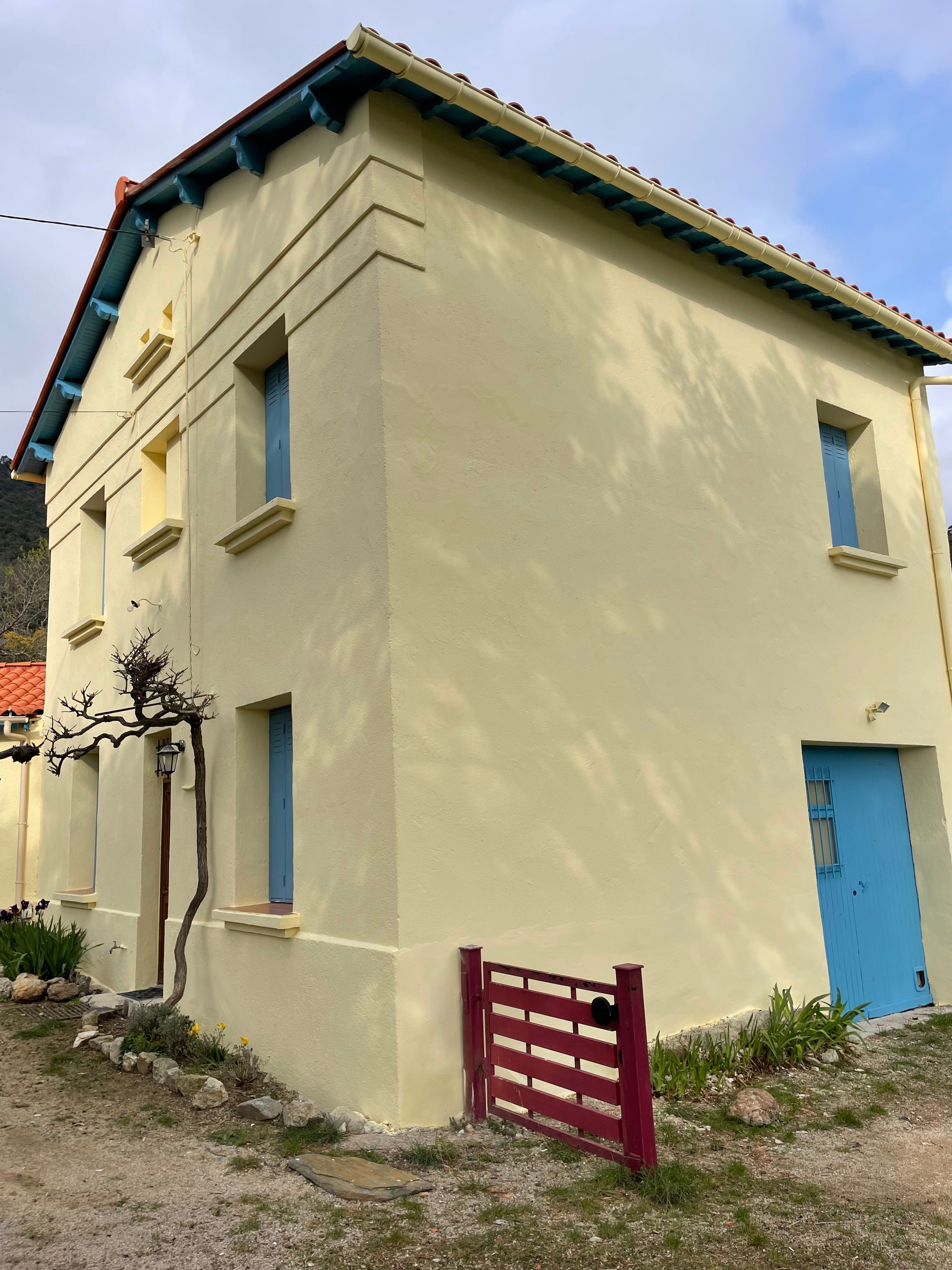 Façade de maison en enduit jaune pâle aux volets bleus, après ravalement