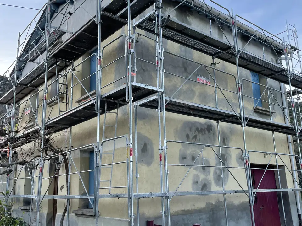 La façade avant travaux, sous échafaudage, enduit marqué de taches et de reprises grises
